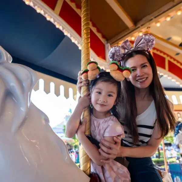 Asian mother and adorable kid daughter riding carousel at theme park.