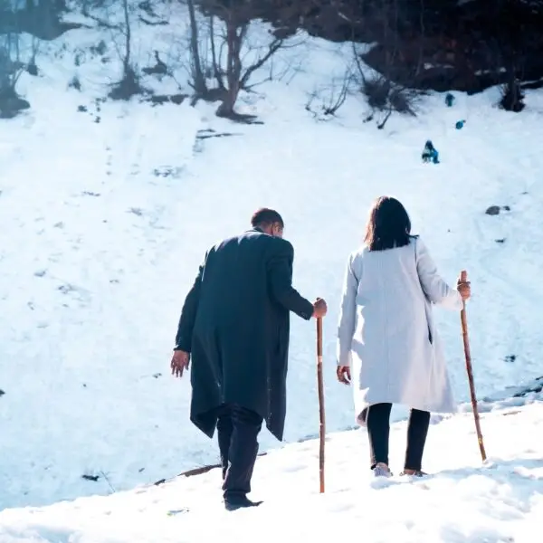 Back view of a couple in coats hiking up the snowy hill in the Solang Valley